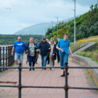 a group of adults walking outdoors along path adjacent to the sea