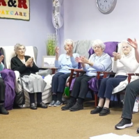 a group of older adults sat indoors clapping together