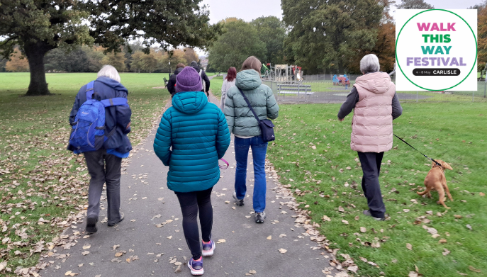 a group of adults walking outdoors in a park.  One of them is holding a dog on a lead