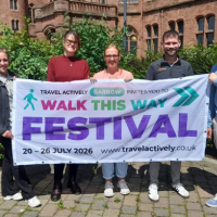 a group of adults standing outdoors holding an advertising banner for Walk This Way Festival
