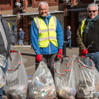 Three men standing outdoors with full bin bags. They are smiling at the camera
