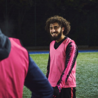 Participant in a pink training bib on a floodlit sports pitch during an evening team training session.