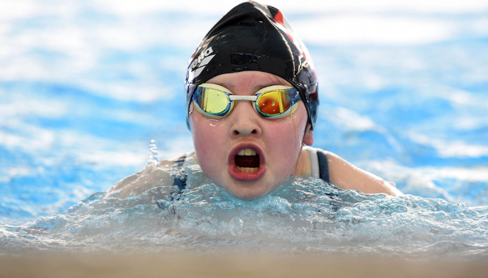 a young girl swimming facing the camera wearing a swim cap