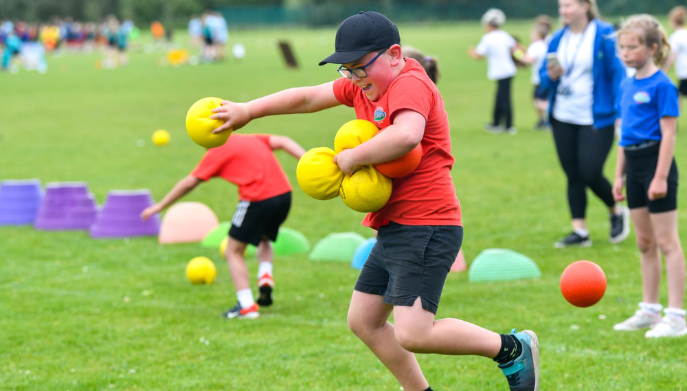 A young boy playing ball outdoors - he is jumping in the air