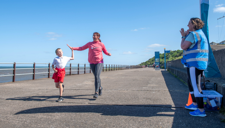 A child and adult running along Maryport Prom. They are doing a 'high-five'