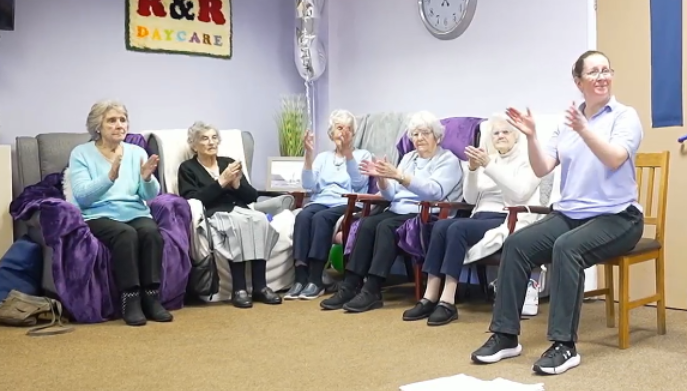 a group of older adults sat indoors clapping together