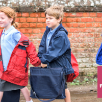 three children - a girl and two boys walking to school.  they are carrying satchels and dressed in school uniform