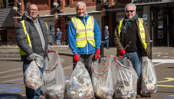 Three men standing outdoors with full bin bags. They are smiling at the camera