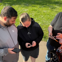 A group of adults standing outdoors looking at a mobile phone