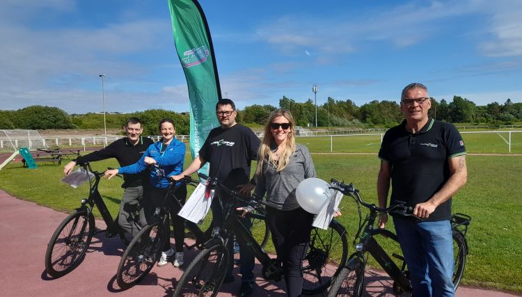 a group of adults stood beside e-bikes outdoors on a cycle track