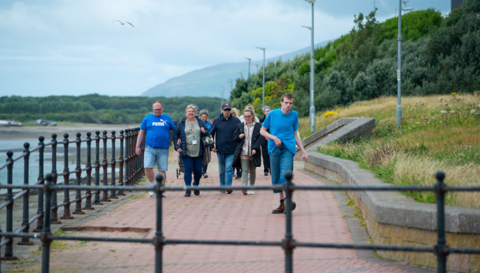 a group of adults walking outdoors along path adjacent to the sea