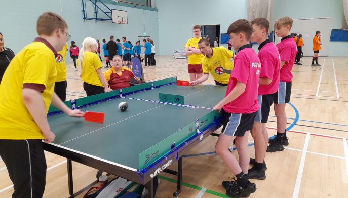 children and young people dressed in yellow and pink t-shirts playing table cricket in a sports hall